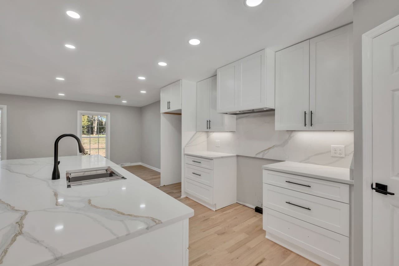 Remodeled white kitchen with quartz countertops, tile backsplash, and island