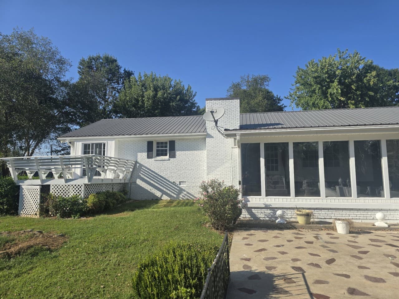 Rear of the residence with lawn, stone patio, deck, and Florida room
